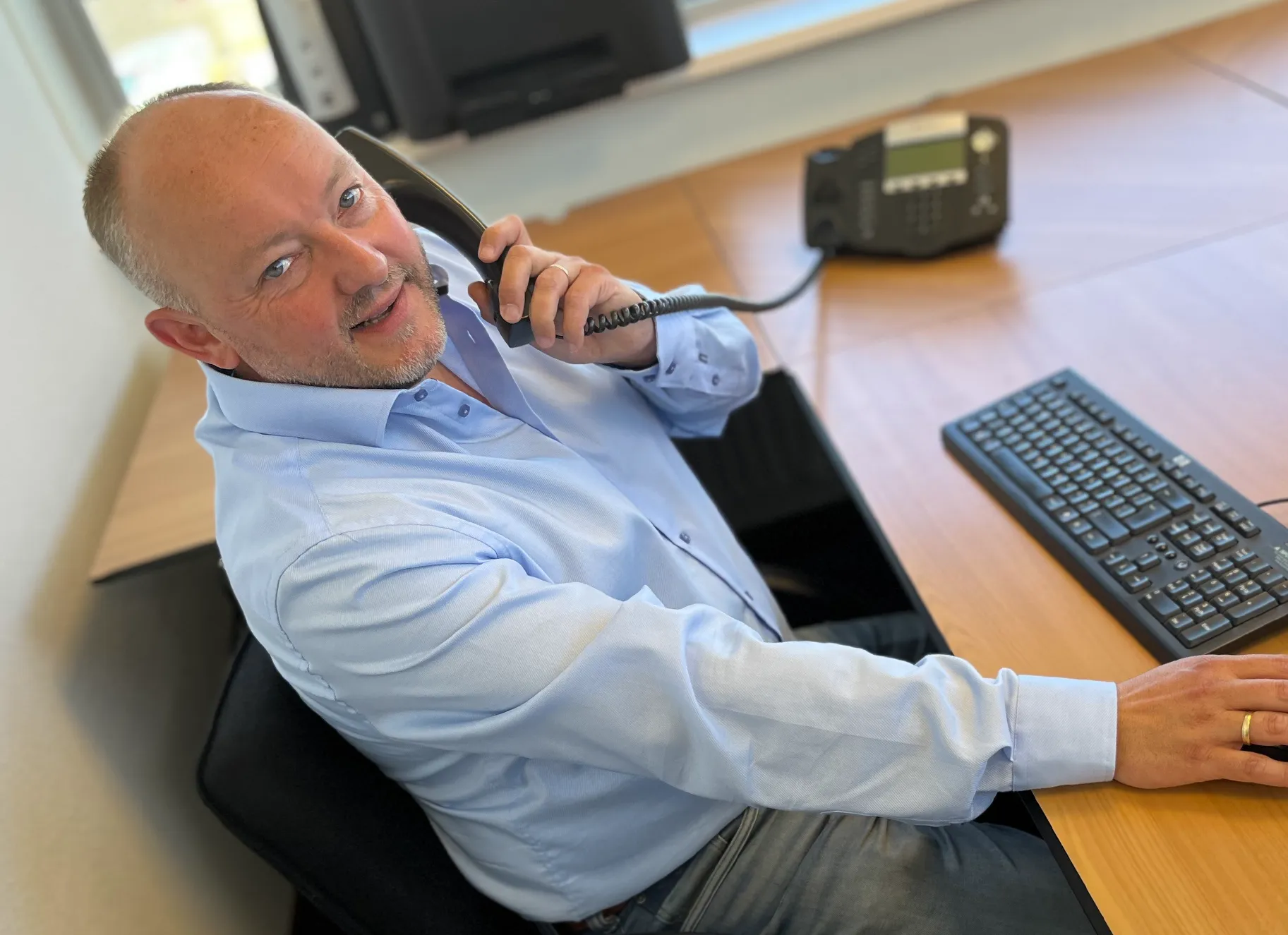 Foto toont Henri zittend achter zijn bureau met de telefoon in zijn hand.
